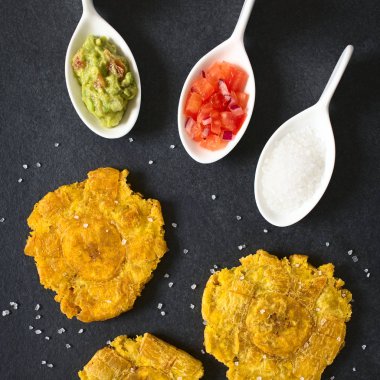 Patacon veya toston, kızarmış ve düzleştirilmiş adet yeşil plantain, geleneksel yiyecek ya da bir eşliğinde Caribbean, guacamole, domates ve soğan salatası, tarafında, tuz ek yükü üzerinde barut doğal ışık ile fotoğrafı