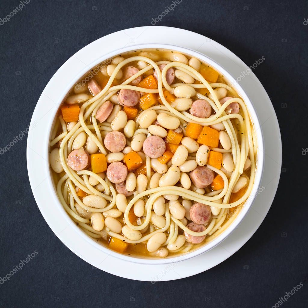 Chilean traditional Porotos con Riendas (beans with reins) dish of cooked dried beans with pumpkin, onion, spaghetti and sausage, photographed overhead on slate with natural light