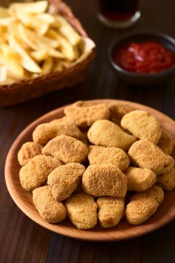 Kotletpane kızarmış gevrek tavuk nuggets ahşap plaka, patates kızartması, ketçap ve meşrubat arkada, üzerinde fotoğrafı üzerinde koyu renkli ahşap doğal ışık (seçici odak, odak üçte biri haline görüntü ile)