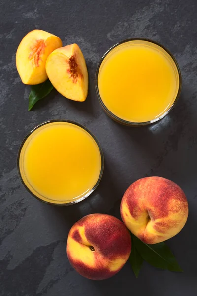 桃汁或花蜜在眼镜与新鲜成熟的桃子水果在旁边 在石板上拍摄与自然光 选择性聚焦 聚焦在果汁的顶部和整个水果的顶部 — 图库照片