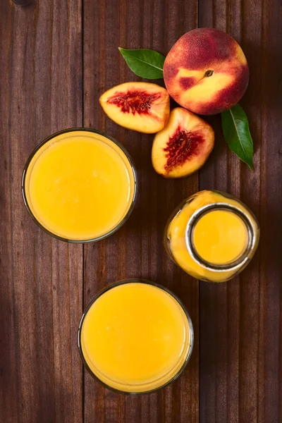 桃汁或花蜜在眼镜和瓶与新鲜成熟的桃子水果在旁边 被拍在黑暗的木头与自然光的头顶 选择性焦点 聚焦在果汁的顶部和整个水果的顶部 — 图库照片
