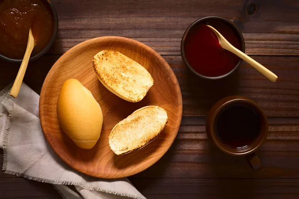 烤面包卷在木盘上 上面有草莓和桃子酱 旁边是质朴的碗和茶 头顶上有自然光的黑木上拍照 — 图库照片