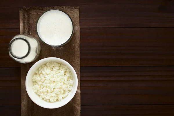 Kefir grains in bowl, fresh kefir drink in glass and a bottle of milk, photographed overhead with natural light (Selective Focus, Focus on the kefir grains and the kefir drink)