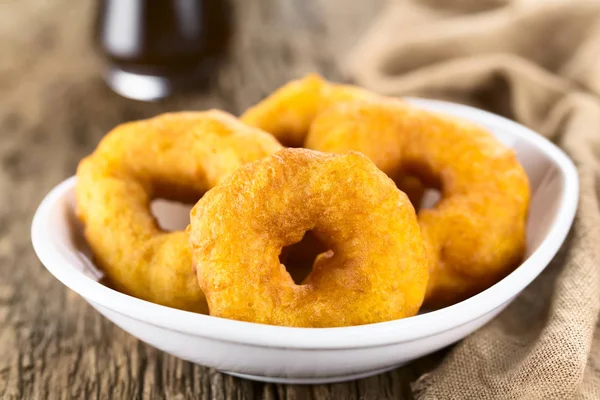 Traditional Chilean Picarones fried pastries made of pumpkin and flour yeast dough, sweet chancaca cane sugar syrup in the back (Selective Focus, Focus on the first picaron)