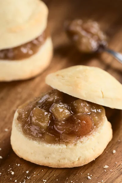 Homemade rhubarb jam on scone, photographed on wooden plate (Selective Focus, Focus on the front of the jam)