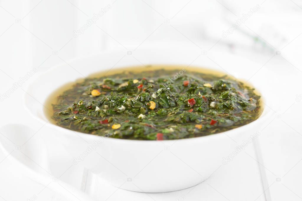 Raw homemade Argentinian green Chimichurri or Chimmichurri salsa or sauce made of parsley, garlic, oregano, hot pepper, olive oil, vinegar, served in bowl, photographed with natural light (Selective Focus, Focus in the middle of the image)