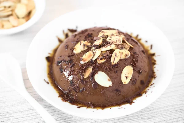 Chocolate pudding or flan dessert with caramel sauce, roasted almond slices and chocolate shavings, photographed with natural light (Selective Focus, Focus in the middle of the dessert)