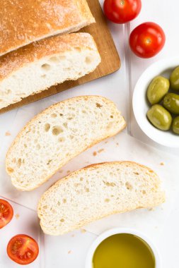 Taze İtalyan ciabatta ekmek dilimlenmiş, kiraz domates ve yeşil zeytin tarafında, beyaz ahşap (Seçici Odak, ekmek dilimleri odaklanın tepegöz üstü fotoğraflandı)