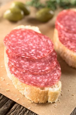 Ciabatta ekmeğine salam dilimleri ve arkasında yeşil zeytinler (Seçici Odak, ikinci salam diliminin önüne odaklan)