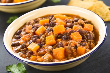 Homemade chili con carne with mincemeat, red and black beans, tomato sauce and pumpkin in enamel bowls, photographed on slate (Selective Focus, Focus one third into the chili) clipart