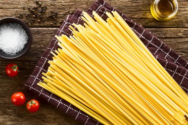 Ham düz uzun kurdele makarna Fettuccini denilen, kiraz domates, tuz, biber ve zeytinyağı tarafında, rustik ahşap üzerinde havai fotoğraflandı