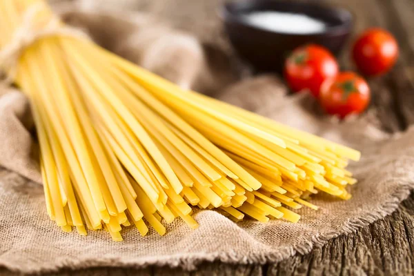 Raw flat long ribbon pasta called Fettuccini, salt and cherry tomatoes in the back (Very Shallow Depth of Field, Focus on the front of the pasta strands)