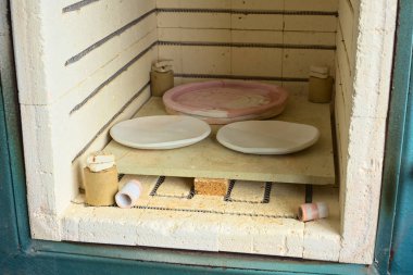 OSORNO, CHILE - SEPTEMBER 16, 2015: Glazed clay pottery in kiln waiting to be fired on September 16, 2015 in Osorno, Chile (Selective Focus, Focus on the front of the first two plates)     clipart