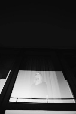 Siyah ve beyaz ruh pencereden bakarak gözlüklü sarışın genç kadın portresi