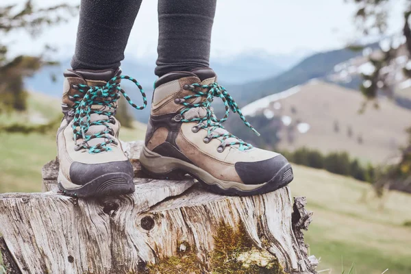 Close up of female classic leather hiking boots wearing by woman standing on stump in mountains - travel and outdoor activities concept