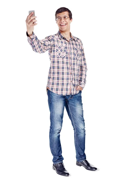 金属フレームのメガネ 格子縞のシャツ ブルー ジーンズ 白い背景の分離された黒い靴を身に着けている携帯電話で Selfie を取って笑顔の若い男の全身肖像画 — ストック写真