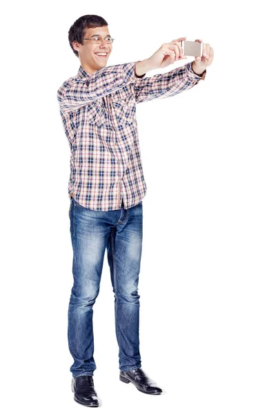 金属フレームのメガネ 格子縞のシャツ ブルー ジーンズ 白い背景の分離された黒い靴を身に着けているスマート フォンで若い男の撮影を笑顔の全身肖像画 — ストック写真