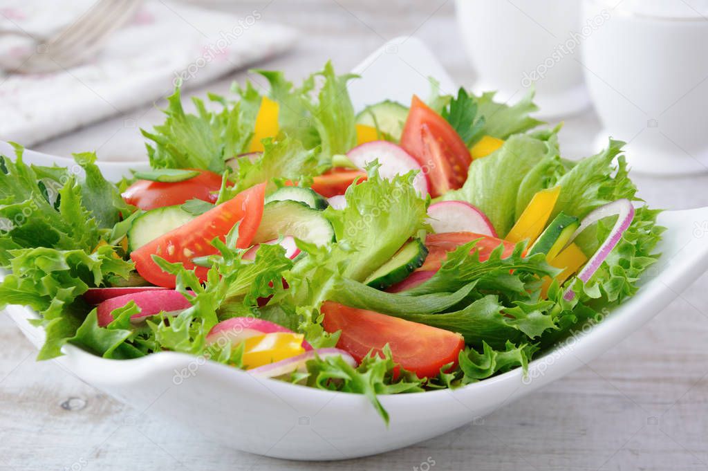 Summer vegetable salad from lettuce leaves with slices of crispy cucumber, tomato slices, radish, seasoned with herbs with fragrant sweet yellow pepper
