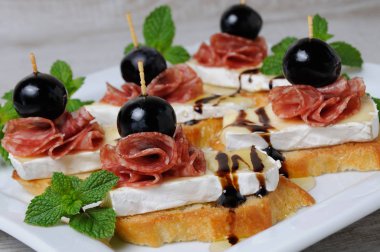 Baget asil beyaz kalıp peynir Brie, altında yumuşak tost dilim üzerinden snack salam, bir dut üzüm bal ile