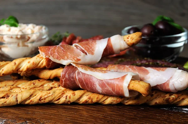  Salam, ekmek sopa (grisini) sarılmış meze aperatifler için çanak prosciutto ile zeytin ve peynir ahşap yüzeyde yapıştırın