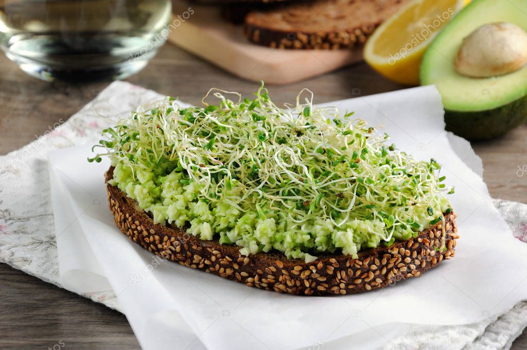 Sandwich of tender, juicy germinated alfalfa and avocado sprouts on slices of rye bread with cereals. This is a great idea for those who watch their health.