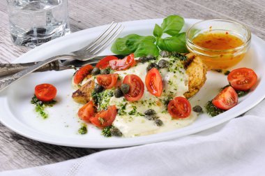 Eritilmiş mozarella peyniri, fesleğen pesto, domates ve kapari soslu ızgara tavuk göğsü.