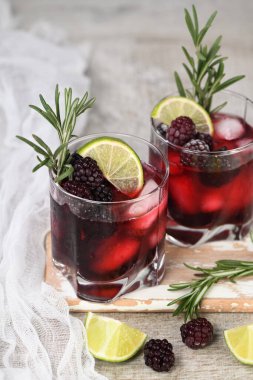Two glasses of delicious refreshing lemonade with blackberry, ice and lime, decorated of rosemary. Cocktail on light table