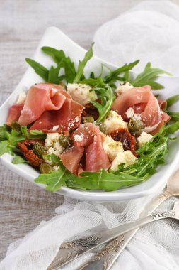 Arugula salatası, güneşte kurutulmuş domatesli jambon, mozzarella dilimleri, kapari zeytinyağı ve parmesanlı baharatlı. Sağlığını gözetleyenler için bir yemek.