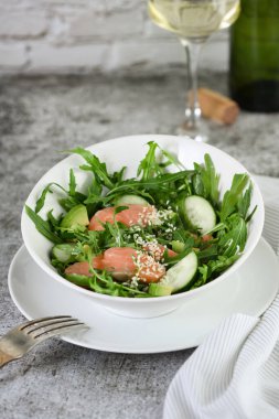 Arugula 'dan sebze salatası, avokado ve salatalık parçaları yanında da taze tuzlu somon ve susam tohumu.