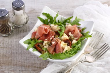 Arugula salatası, güneşte kurutulmuş domatesli jambon, mozzarella dilimleri, kapari zeytinyağı ve parmesanlı baharatlı. Sağlığını gözetleyenler için bir yemek.