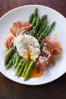 Parmesanlı Benedict usulü yumurta, yeşil kuşkonmaz ve Parma jambonu..