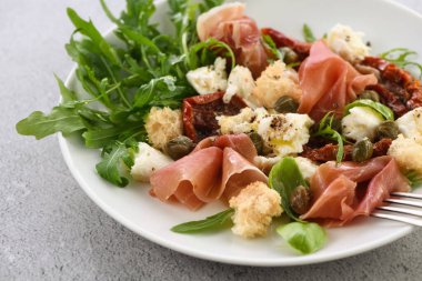 Salata roka, güneşte kurutulmuş domatesli Parma jambonu, mozzarella dilimleri, kızarmış ekmek, kapari, baharat