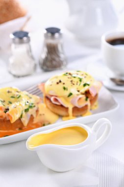 Kahvaltıda soslu Hollandaise tereyağı sosu yanında Benedict usulü yumurta, jambon, haşlanmış yumurta ve bir fincan kahve.