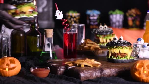 魔女はハロウィーンのパーティーテーブルに面白いモンスターブラックバーガーを提供しています 左から右に移動します リアルタイム — ストック動画