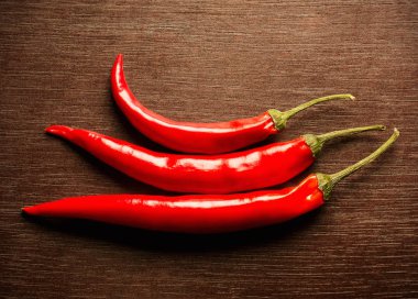 Ahşap arka plan üzerinde kırmızı sıcak biber biber. Üstten görünüm arka plan. Piramit üç taze kırmızı biber vardır