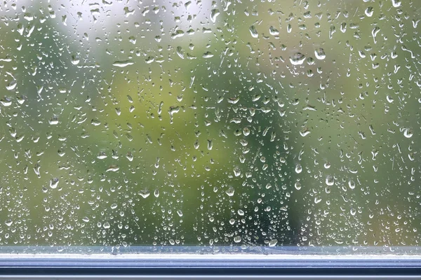 Still-life with with rain droplets on window glass on gloomy autumn day on blur green background closeup