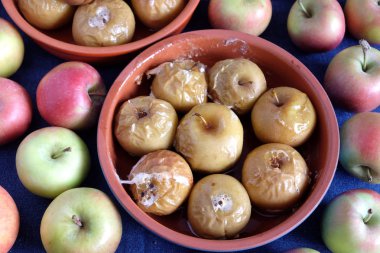 Yuvarlak kil kase ve olgun taze elma closeup çevresinde mavi masa örtüsü üzerinde çok pişmiş elma