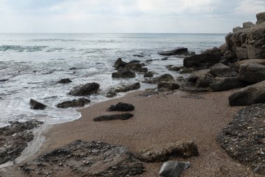 İle kıyı taşlarının üzerinde bulutlu hava çalıştıran dalgalar deniz manzara