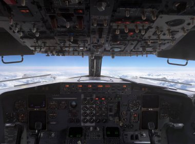 Uçak, mavi gökyüzündeki beyaz bulutların üzerinde uçuyor ve pilotkabininden ufuk çizgisine doğru uçuyor.