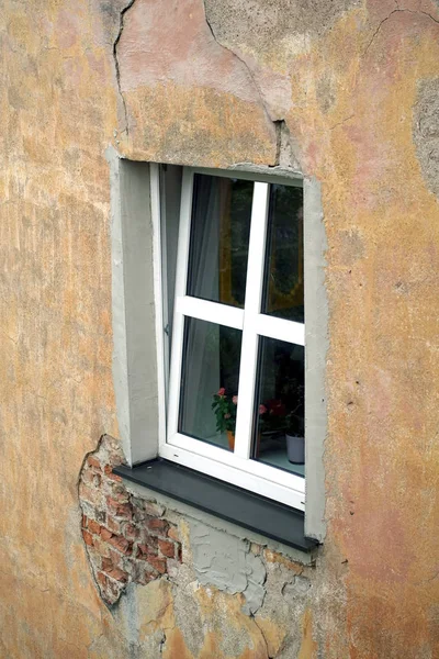 一个打开的新塑料窗口与白色框架在破旧的房子墙壁上覆盖着石膏侧视图垂直特写 — 图库照片