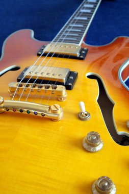 Eski usul yarı-akustik, yarı içi boş caz elektro gitar, altın pikaplar, elektronik düğmeler ve metal aksesuarlar mavi pamuk arka planda dikey fotoğraf.