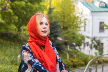 Yaz aylarında yeşil ağaçların arka planında kırmızı fularlı orta yaşlı güzel bir kadın. Bahar kavramı, kadınlık.