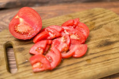 Bir bıçak ile doğrama tahtası üzerinde dilimlenmiş kırmızı domates.