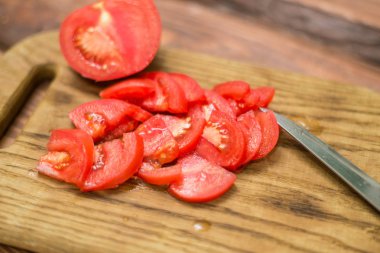 Bir bıçak ile doğrama tahtası üzerinde dilimlenmiş kırmızı domates.