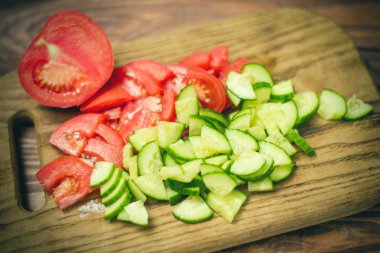 Tahta bir tahta üzerinde dilimlenmiş taze domates ve salatalık. Sebze salatası pişiriyorum. Sağlıklı, vegan gıda kavramı.