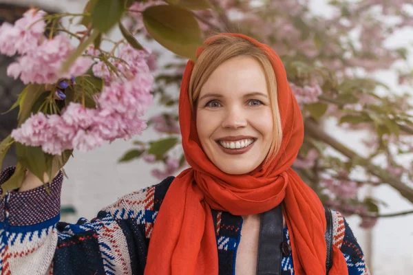 Beautiful middle-aged woman in a red scarf on a background of green trees in the summer. The concept of spring, femininity.