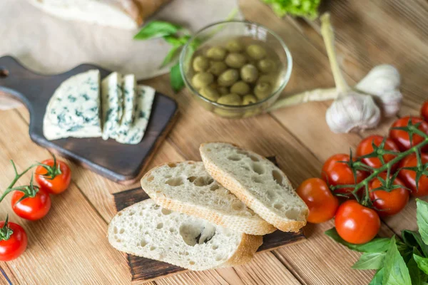 Bruschetta pişirme için Malzemeler: doğranmış ciabatta, zeytin, domates, ahşap bir arka plan üzerinde mavi peynir. Sağlıklı ve lezzetli yemekler pişirme.