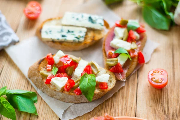 Tradycyjny włoski bruschetta z niebieskim serem, feta, pomidory, liście bazylii, Jamon na drewnianym tle. — Zdjęcie stockowe
