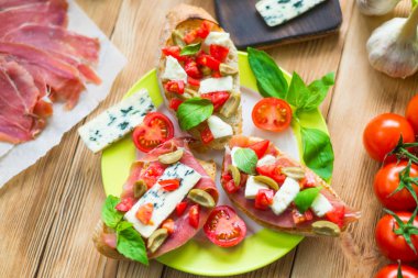 Mavi peynir, beyaz peynir, domates, fesleğen yaprakları, ahşap bir arka plan üzerinde jamon ile Geleneksel İtalyan bruschetta.