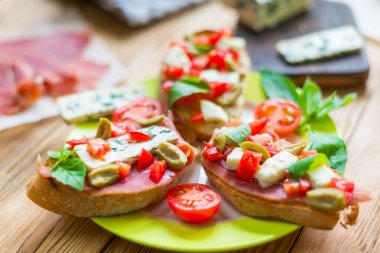 Mavi peynir, beyaz peynir, domates, fesleğen yaprakları, ahşap bir arka plan üzerinde jamon ile Geleneksel İtalyan bruschetta.